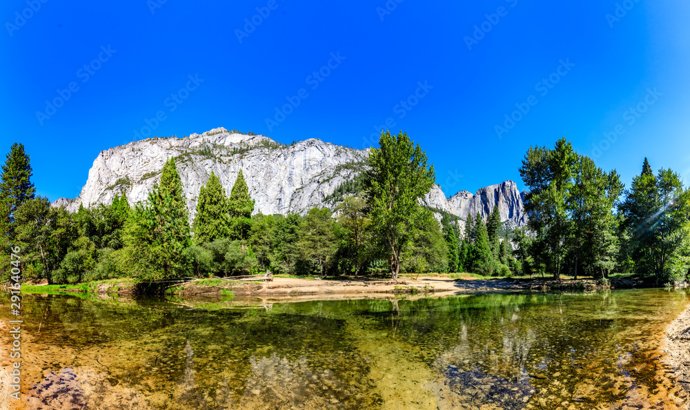 The clean flat Merced river reflects trees in the foreground and the tall granite of Eagle Peak in Yosemite National Park