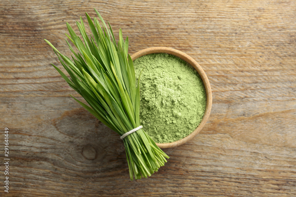 Bowl of wheat grass powder and green sprouts on wooden table, flat lay Bowl of wheat grass powder and green sprouts on wooden table, flat lay