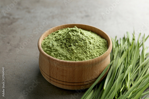 Wooden bowl of wheat grass powder and sprouts on grey table
