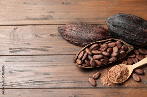 Flat lay composition with cocoa pods, beans and powder on wooden table, space for text