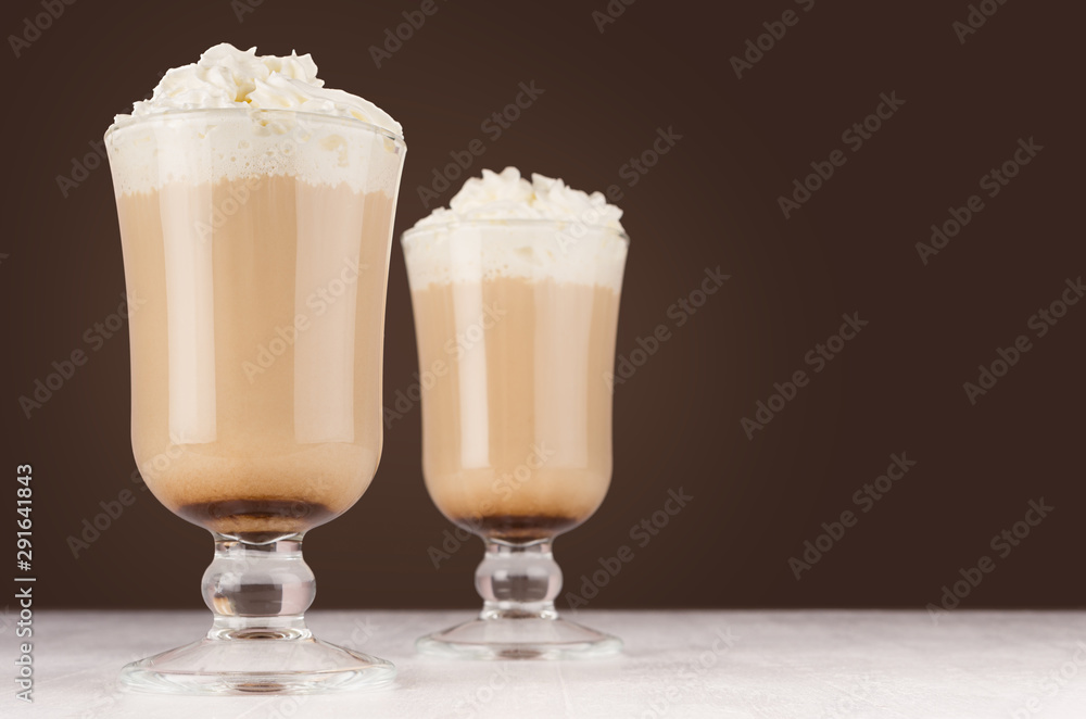 Two hot coffee drinks with whipped cream in wineglass in dark brown interior on white wooden table, copy space. Two hot coffee drinks with whipped cream in wineglass in dark brown interior on white wooden table, copy space.
