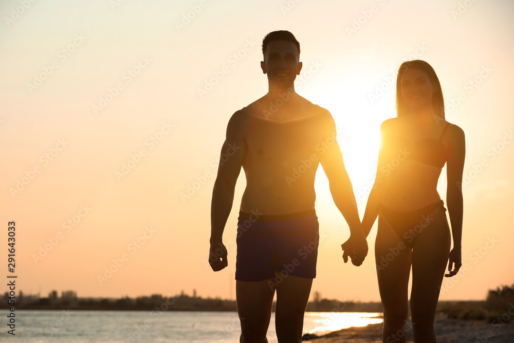 Young woman in bikini spending time with her boyfriend on beach at sunset. Lovely couple