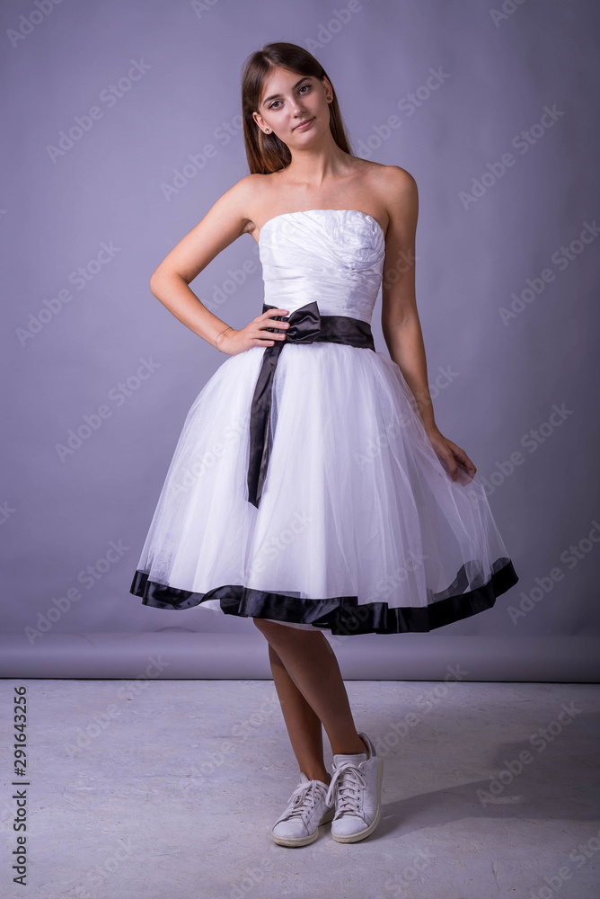 Naklejka premium Young beautiful female model in white dress on gray background. Beautiful girl in an airy dress.
