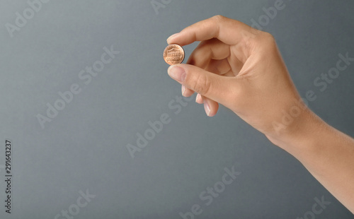 Young woman holding coin on grey background, closeup. Space for text