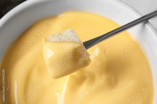 Dipping bread into tasty cheese fondue, closeup