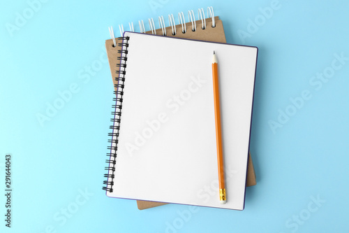 Notebooks with pencil on light blue background, top view