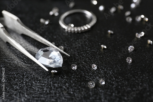 Jewels and tweezers on black leather surface
