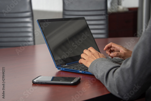 manos de mujer morena trabajadora con telefono celular y laptop azul en oficina