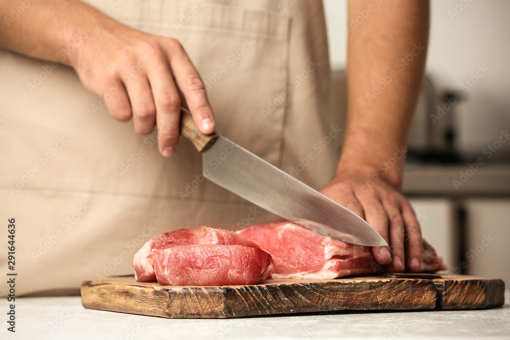 Man cutting fresh raw meat on table in kitchen, closeup