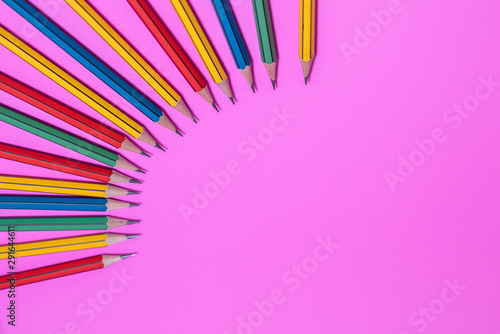 A variety of colored pencils arranged in a circle on a beautiful pink background
