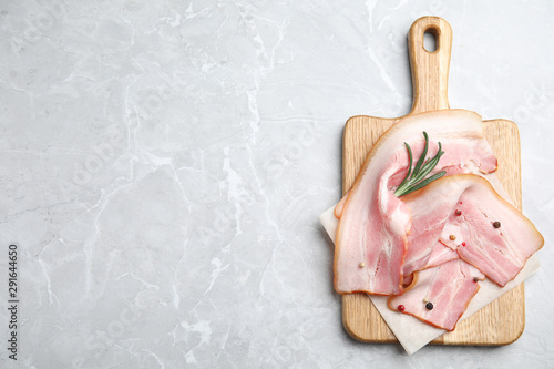 Photography Wooden board with sliced raw bacon on light grey marble table, top view