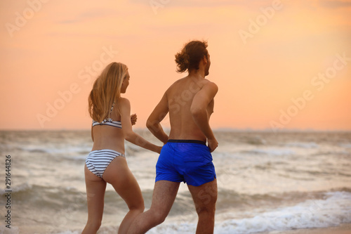 Young woman in bikini and her boyfriend walking on beach at sunset. Lovely couple © New Africa