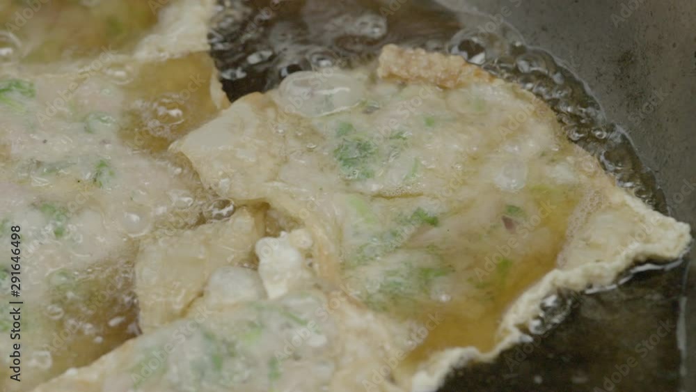 A slow-motion, closeup shot of pieces of fried tempura with minced meat and veggies on the inside being cooked in a frying pan filled with boiling hot oil. A slow-motion, closeup shot of pieces of fried tempura with minced meat and veggies on the inside being cooked in a frying pan filled with boiling hot oil.