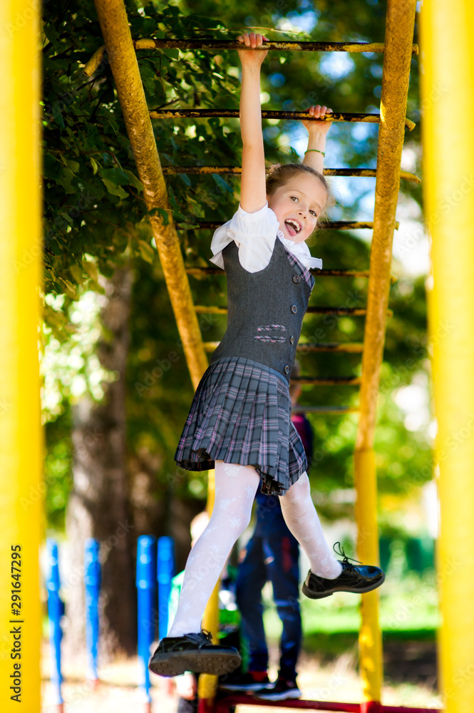 Fototapeta premium Girl schoolgirl in a school uniform climbs a sports horizontal bar