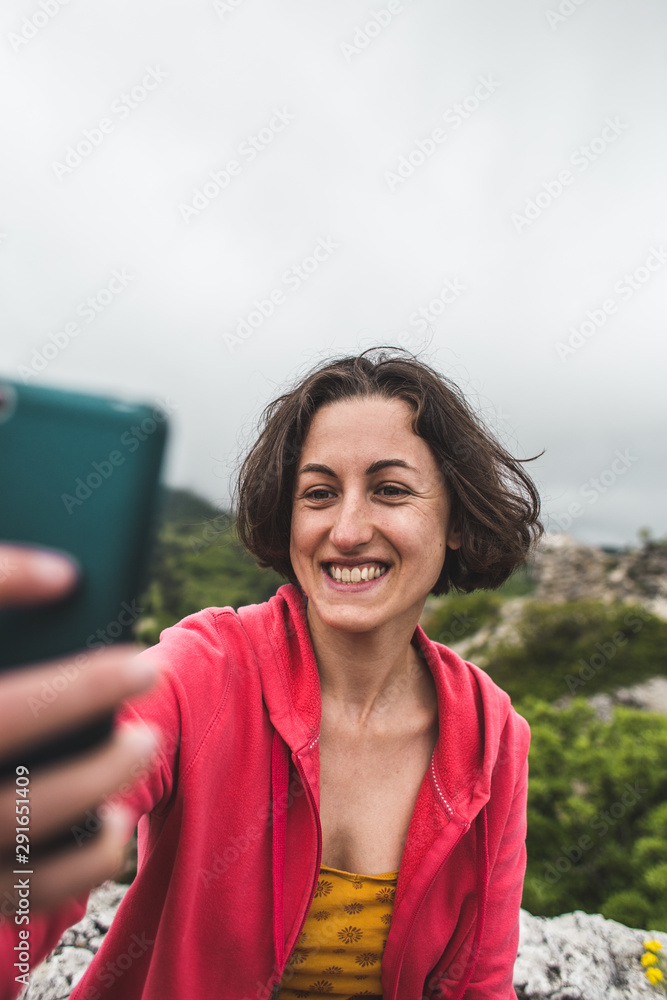 A woman takes a selfie on top of a mountain.