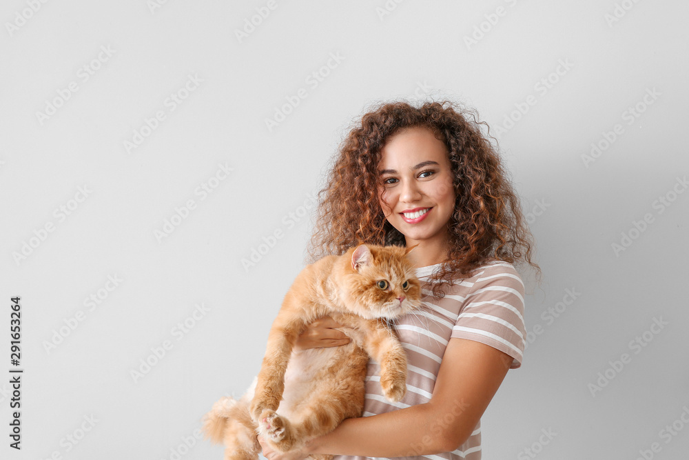 Young African-American woman with cute cat on light background Young African-American woman with cute cat on light background