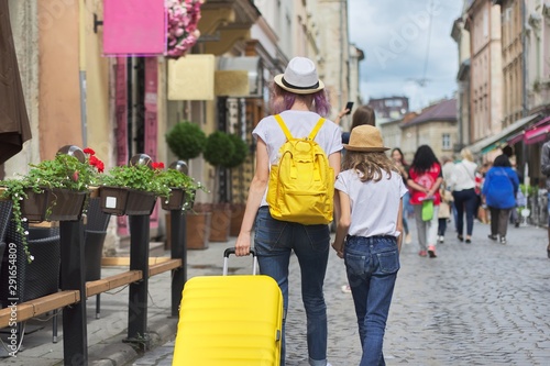 Two girls walking in city with suitcase, back view