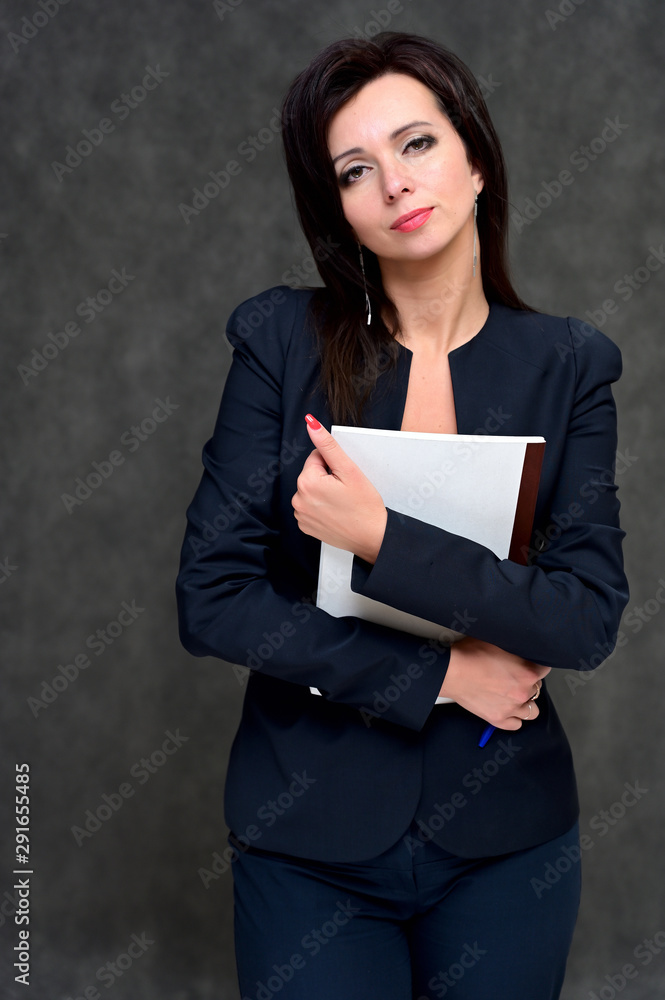Naklejka premium Portrait of a brunette manager woman in a business suit on a gray background. Great makeup and beautiful hair. Standing right in front of the camera in various poses.
