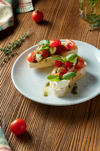 bruschetta with cherry tomatoes, basil, pesto sauce and mozzarella on a white plate on a wooden background. Italian restaurant. Top view food photo