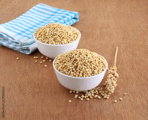 Sorghum, also known as jowar, which is a whole grain and a healthy food, in bowls, and its stalk, on a wooden background.