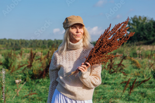 Happy beautiful blond woman walking in a green field with a bouquete of dry brown plants