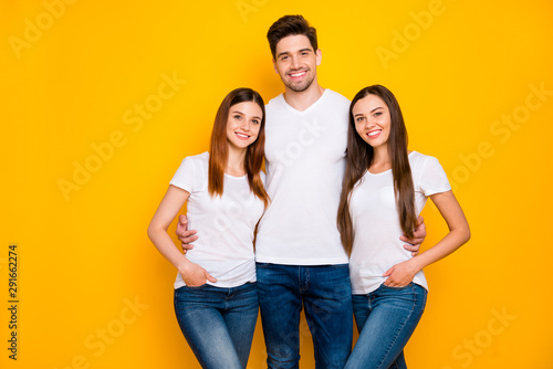 Portrait of charming fellows looking at camera with beaming smile wearing white t-shirt denim jeans isolated over yellow background