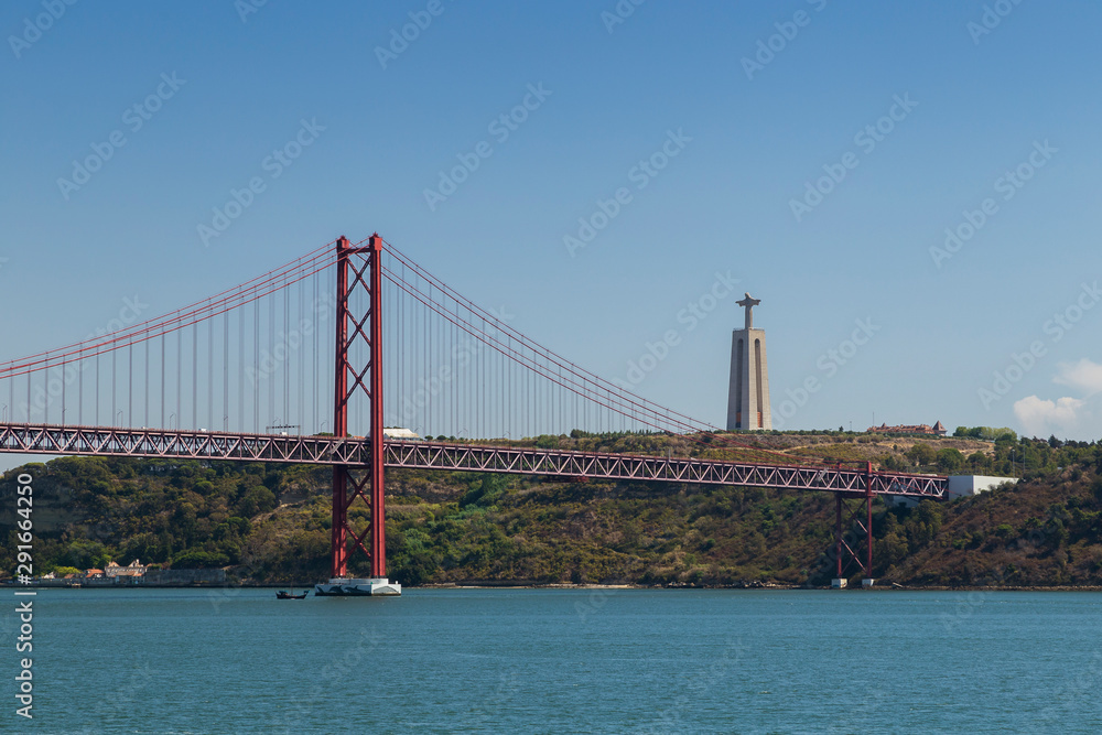 Naklejka premium Tagus River, 25 de Abril Bridge (Ponte 25 de Abril, 25th of April Bridge) and Sanctuary of Christ the King (Santuario de Cristo Rei) monument in Lisbon, Portugal, on a sunny day.