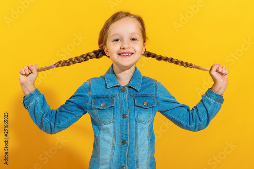 Canvastavla Portrait of a cheerful little girl in a denim shirt on a yellow background