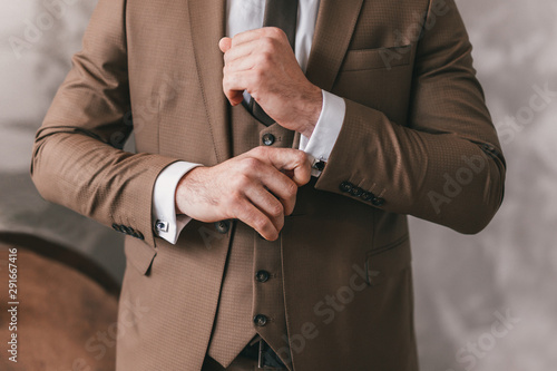 Elegant young fashion man looking at his cufflinks while fixing them. Black and white photo of male hands. Handsome groom dressed in black formal suit, white shirt and tie is getting ready for wedding photo