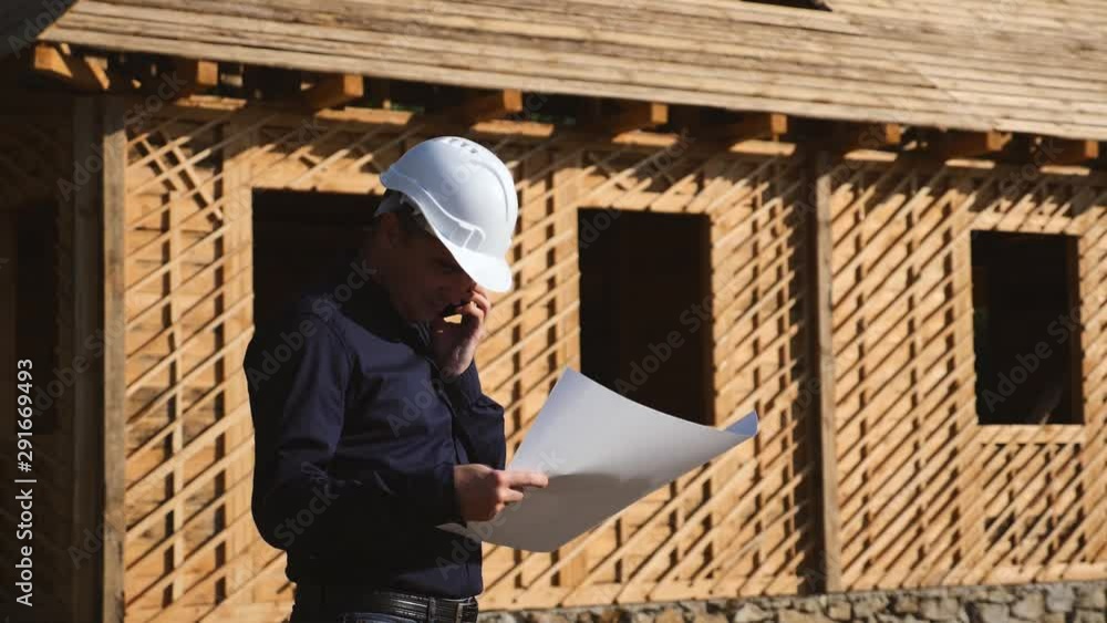 An engineer in a white helmet is considering a project to build a house made of natural materials. Modern technologies of construction of environmentally friendly material. An engineer in a white helmet is considering a project to build a house made of natural materials. Modern technologies of construction of environmentally friendly material.