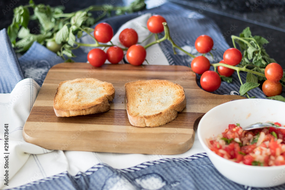 Ingredients for making a bruschetta, with rustic bread, cherry tomatoes, parsley and onion with olive oil on the wooden board. Variation of a traditional italian appetizer or snack, antipast Ingredients for making a bruschetta, with rustic bread, cherry tomatoes, parsley and onion with olive oil on the wooden board. Variation of a traditional italian appetizer or snack, antipast