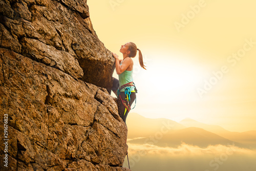 Beautiful Woman Climbing on the Rock at Foggy Sunset in the Mountains. Adventure and Extreme Sport Concept