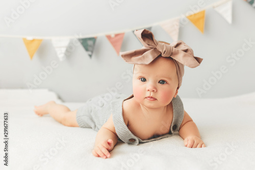 Beautiful baby lies on bed smiling bow on her head. photo