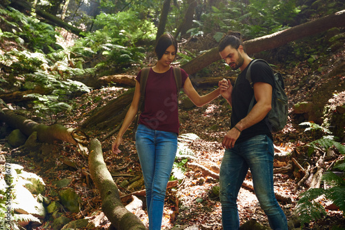 Couple negotiating a steep path over a fallen tree