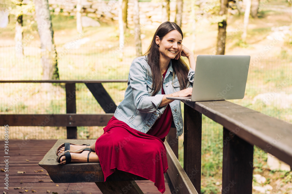 Happy smiling young brunette girl with laptop on a park background. Freelancer at work in the fresh air. Happy smiling young brunette girl with laptop on a park background. Freelancer at work in the fresh air.