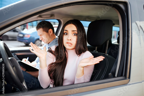 Male auto instructor takes exam in young woman. Sit beside model in car and write down. Young woman look confused on camera and show hands. Stress and failing exams. © estradaanton