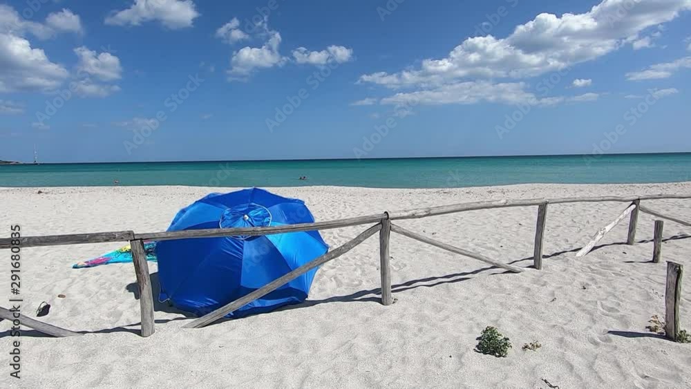 Deserted white beach with a blue beach umbrella seen from behind that flutters in the wind against a background of blue sea and sky Deserted white beach with a blue beach umbrella seen from behind that flutters in the wind against a background of blue sea and sky