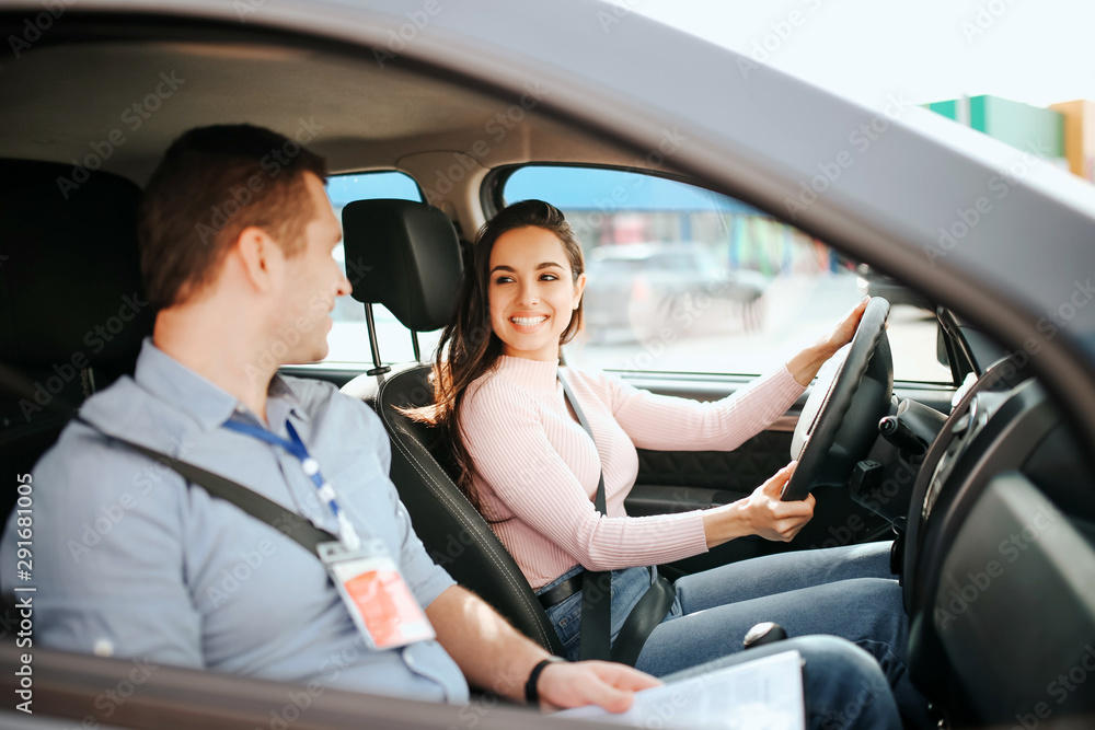 Male auto instructor takes exam in young woman. Cheerful attractive and positive model look at guy and smile. Drive car with confidence.