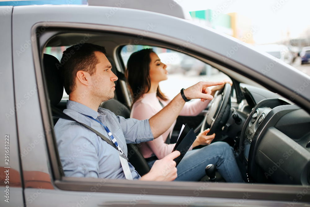 Male auto instructor takes exam in young woman. Careful driving and passing practical test. Instructor help with driving. Young woman pass test with confidence and very careful.