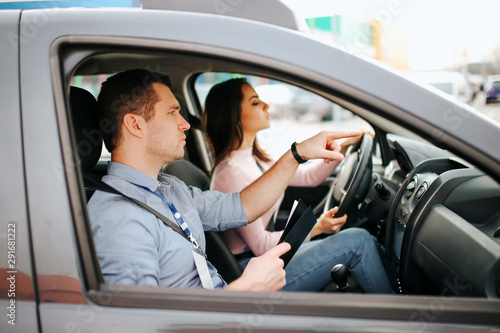 Male auto instructor takes exam in young woman. Careful driving and passing practical test. Instructor help with driving. Young woman pass test with confidence and very careful. © estradaanton