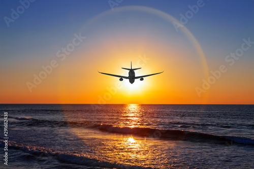 Silhouette of an airplane on the background of halo over the sea at sunset