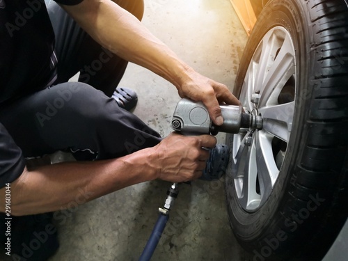 Removing car mechanic to repair the leaky tire car wheels.Mechanic changing a car tire on a vehicle a hoist using an electric drill to loosen the bolts .concept of service or replacement. © Chinnabanchon