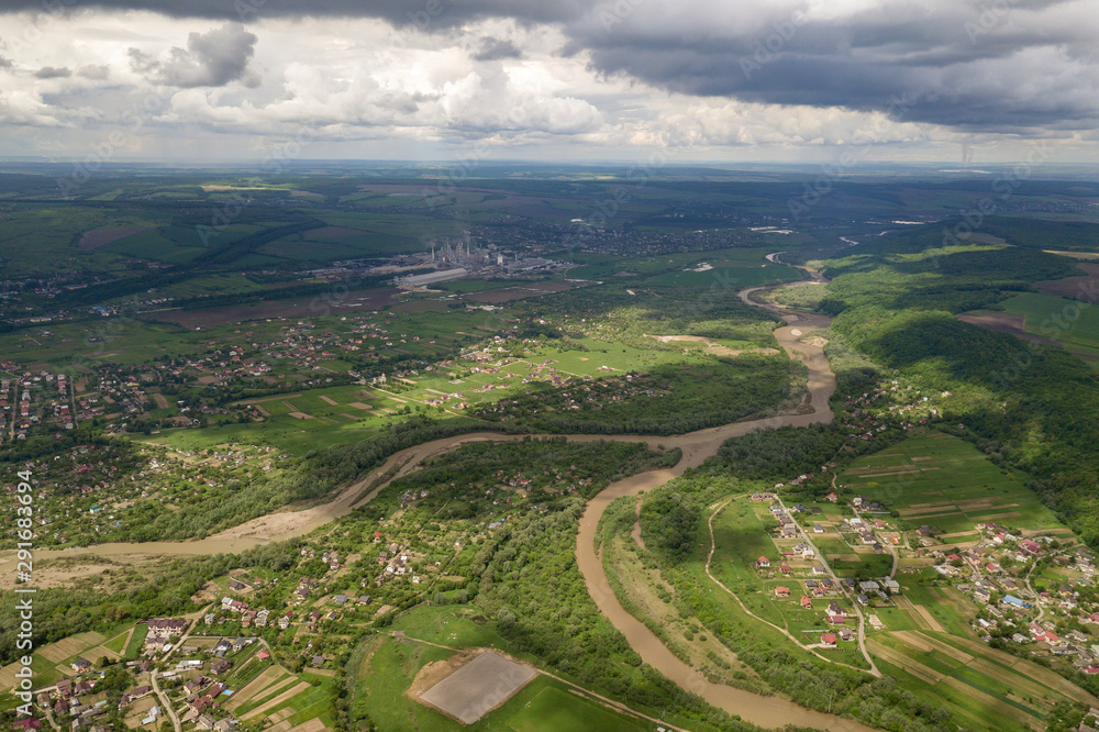 Aerial view of town or village with rows of buildings and curvy streets between green fields in summer. Countryside landscape from above.