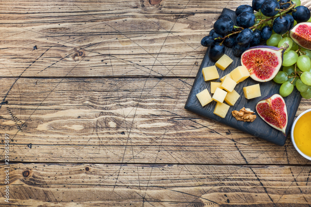 Cheese cubes, fresh fruit figs grapes Honey walnut on wooden chopping Board. Copy space.