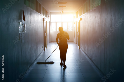 Janitor woman mopping floor in hallway office building or walkway after school and classroom silhouette work job with sun light background. photo