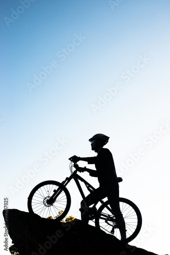 Silhouette of the athlete standing on the rock with bicycle