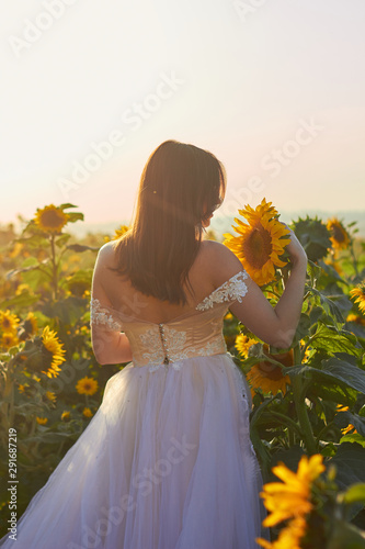 Beautiful young girl in a white dress enjoying nature on a field of sunflowers. Sunlight plays on the field. Outdoor lifestyle.Amazing view and nature.