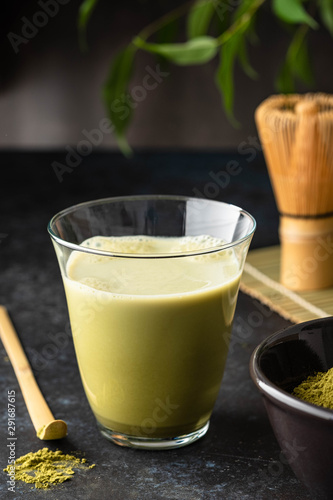 Matcha green tea latte in glass mug with whisk.
