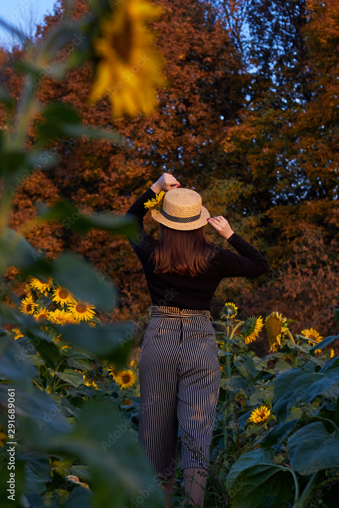 Beautiful lovely girl in a straw hat enjoying nature on a field of sunflowers. Sunset. Autumn time
