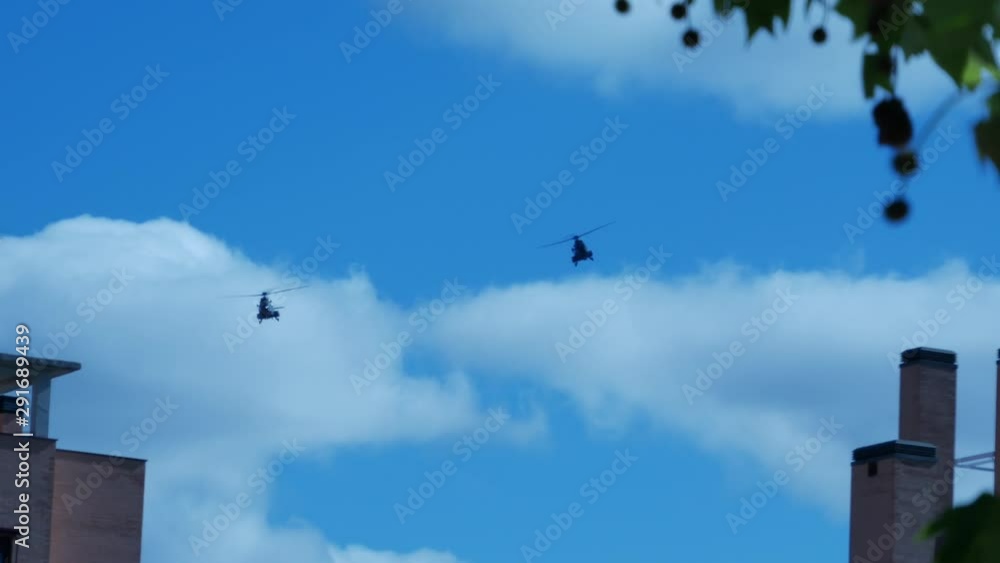 Two militar helicopters flying over a city, appearing behind a building Two militar helicopters flying over a city, appearing behind a building